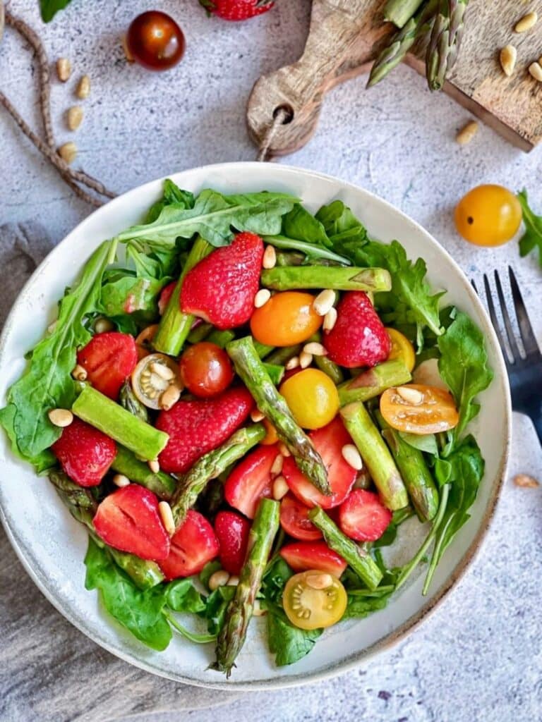 Spargelsalat mit Erdbeeren, Rucola und Pinienkerne auf einem Teller.