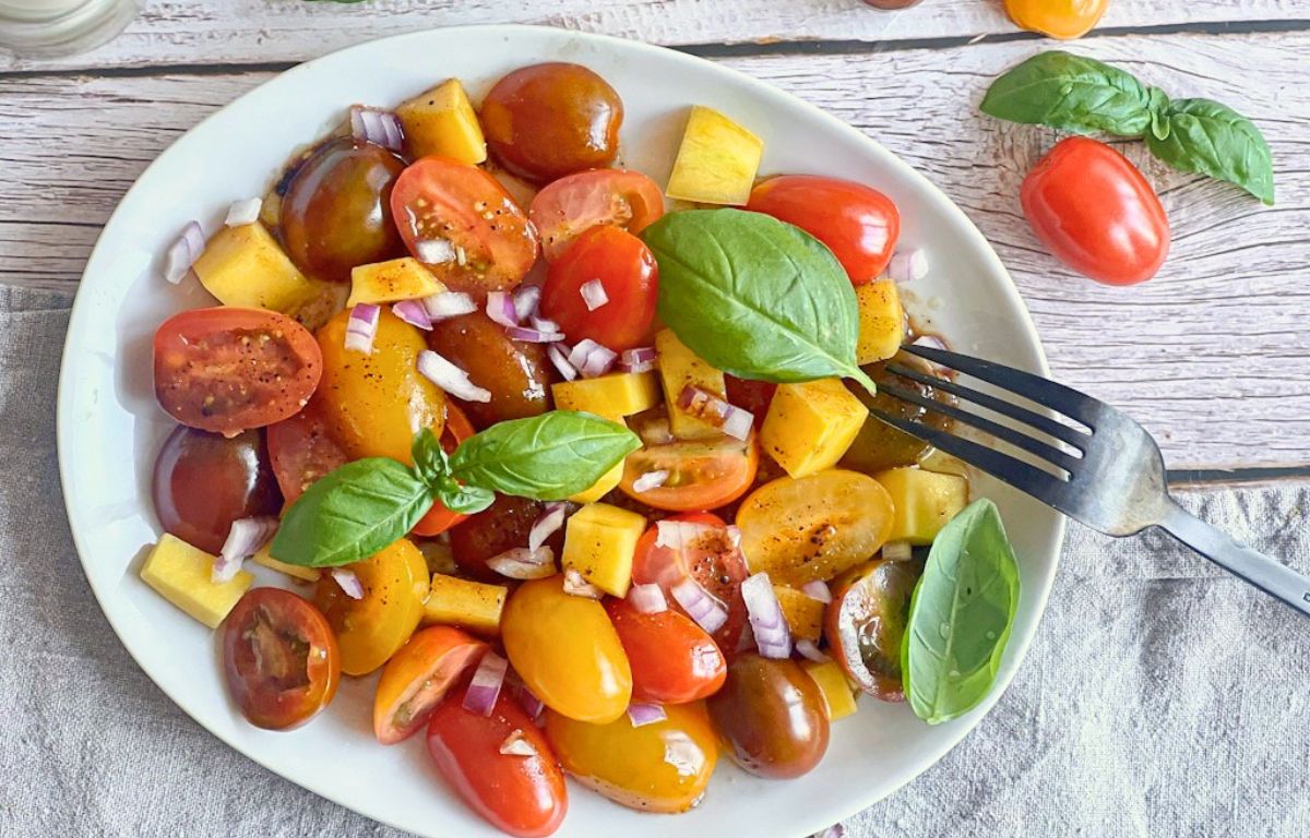Veganer Tomaten-Mango-Salat mit Zwiebeln und Basilikum auf einem Teller.