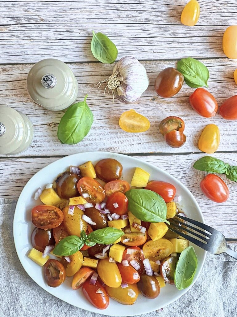 Veganer Tomaten-Mango-Salat mit Basilikum auf einem Teller.