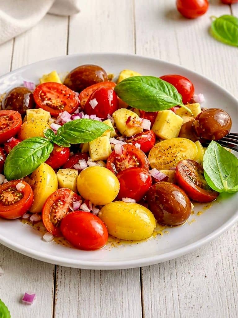 Veganer Tomaten-Mango-Salat mit Zwiebeln und Basilikum auf einem Teller.
