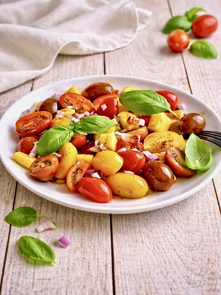 Veganer Tomaten-Mango-Salat mit Zwiebeln und Basilikum auf einem Teller.