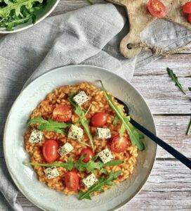 Einfaches Tomatenrisotto mit Rucola und Kräutertofu auf einem Teller.