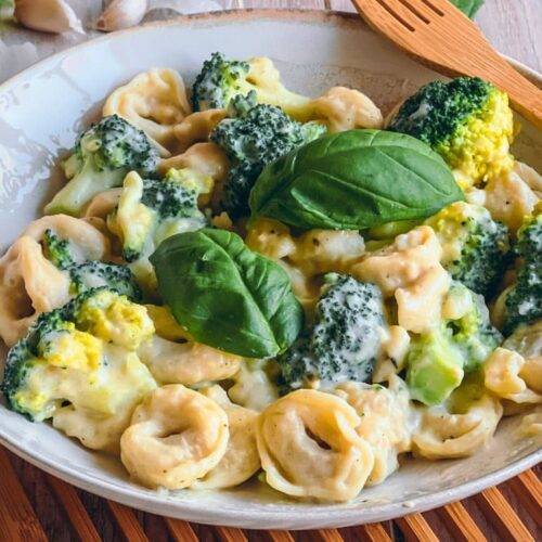 Vegane Tortellini mit Brokkoli in Käsesoße auf einem Teller auf einem Holzbrett.