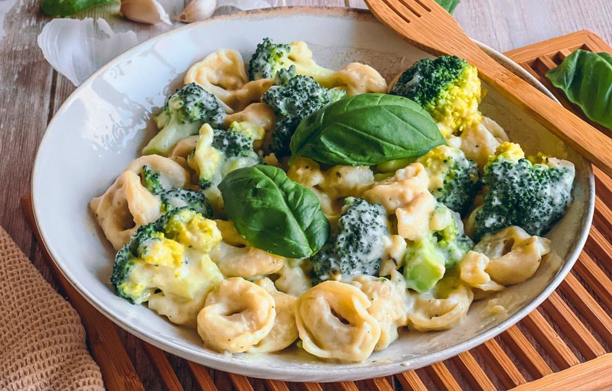 Vegane Tortellini mit Brokkoli in Käsesoße auf einem Teller auf einem Holzbrett.