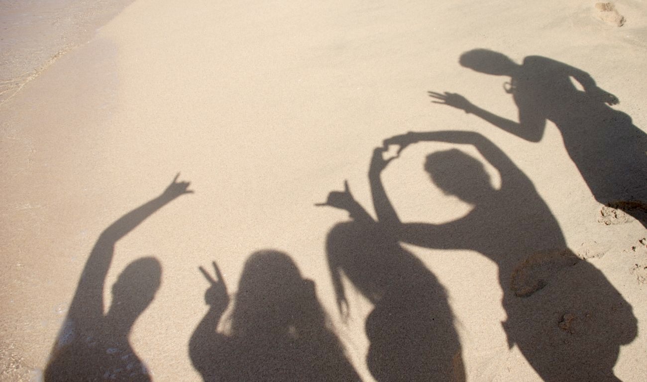 Schatten von Menschen am Strand, die ihre Freundschaft durch Handzeichen bekunden.