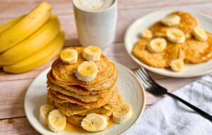 Vegane Bananen-Pancakes mit Ahornsirup gestapelt auf einem Teller.