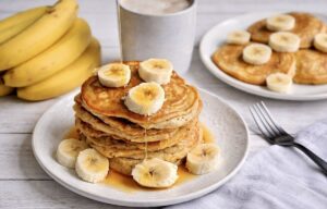 Vegane Bananen-Pancakes mit Ahornsirup gestapelt auf einem Teller.