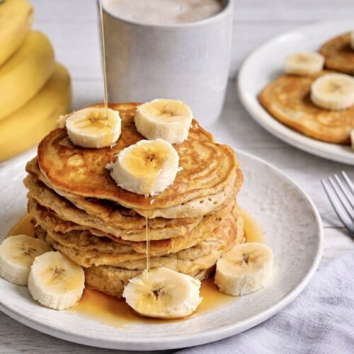 Vegane Bananen-Pancakes mit Ahornsirup gestapelt auf einem Teller.