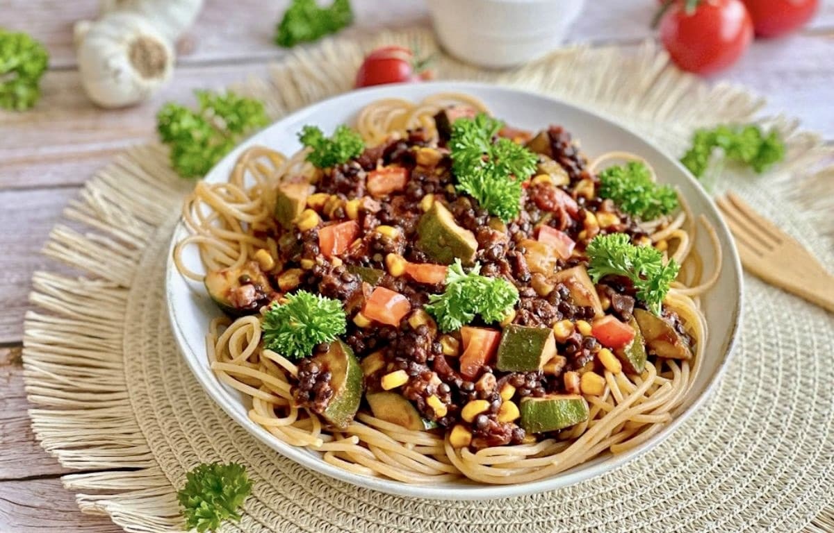 Vegane Beluga-Bolognese mit Gemüse und Spaghetti auf einem Teller.