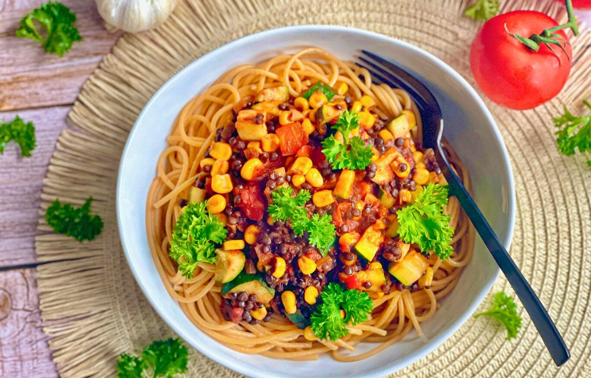 Vegane Beluga-Bolognese mit Gemüse und Spaghetti auf einem Teller.