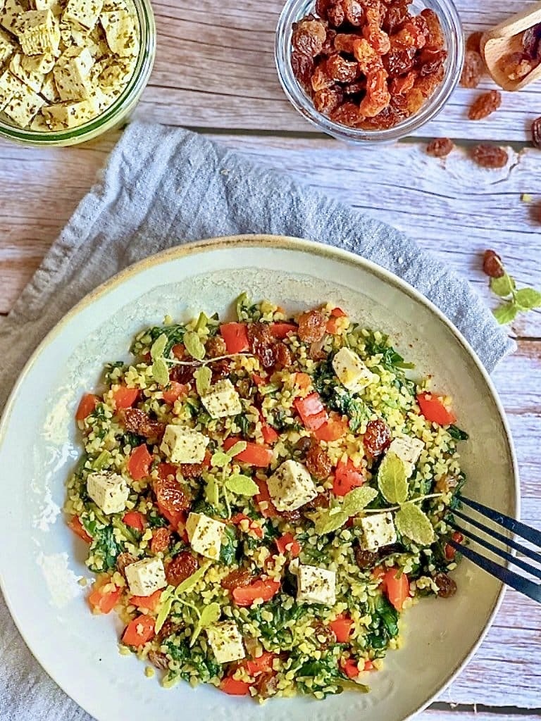 Vegane Bulgurpfanne mit Spinat, Paprika, Rosinen und Kräutertofu auf einem Teller platziert.