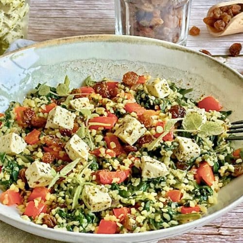 Vegane Bulgurpfanne mit Spinat, Paprika, Rosinen und Kräutertofu auf einem Teller platziert.