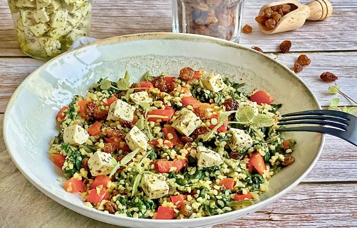 Vegane Bulgurpfanne mit Spinat, Paprika, Rosinen und Kräutertofu auf einem Teller platziert.