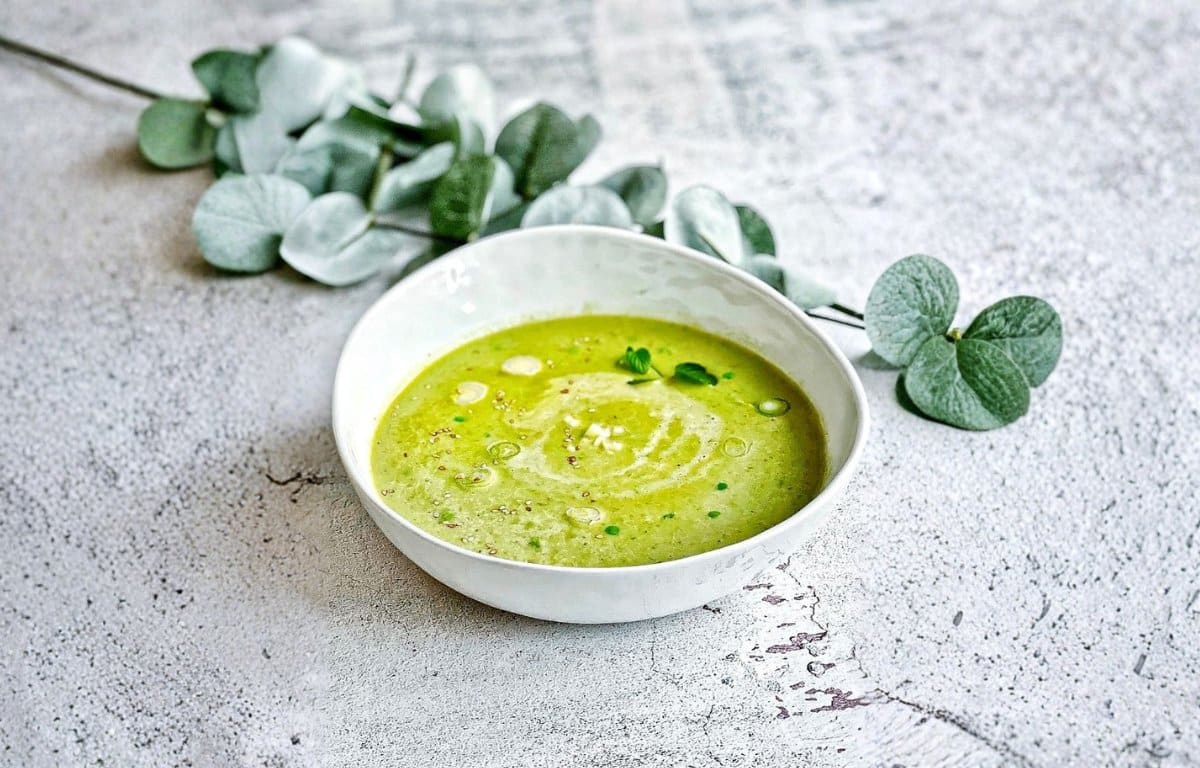 Vegane Erbsensuppe mit Kokosmilch, Minze, Sesam und Lauchzwiebeln in einem Suppenteller.