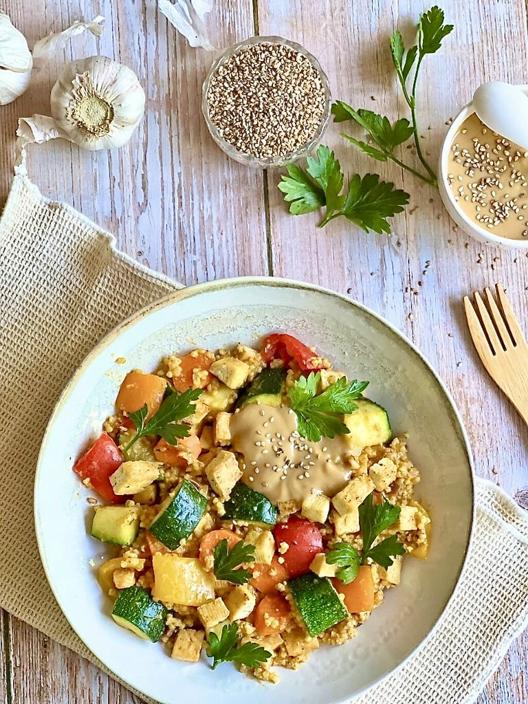 Vegane Hirsepfanne mit Gemüse, Tofu und einer cremigen Tahin-Zitronen-Soße auf einem Teller.