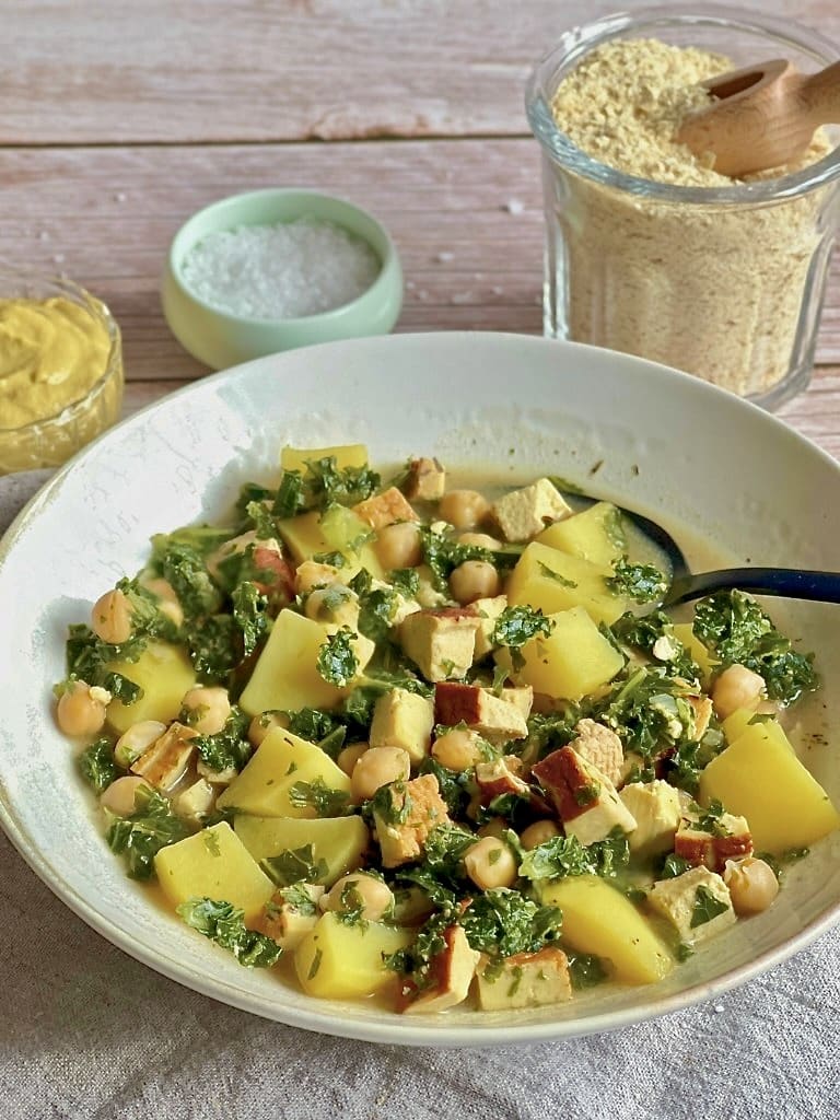 Veganer Kartoffel-Grünkohl-Eintopf mit Räuchertofu und Kichererbsen in einem Suppenteller.