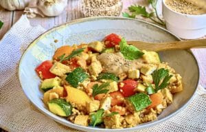 Vegane Hirsepfanne mit Gemüse, Tofu und einer cremigen Tahin-Zitronen-Soße auf einem Teller.