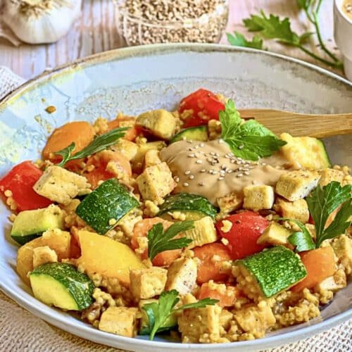 Vegane Hirsepfanne mit Gemüse, Tofu und einer cremigen Tahin-Zitronen-Soße auf einem Teller.