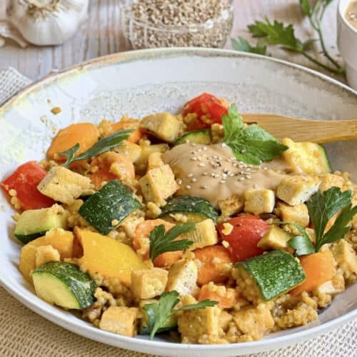 Vegane Hirsepfanne mit Gemüse, Tofu und einer cremigen Tahin-Zitronen-Soße auf einem Teller.