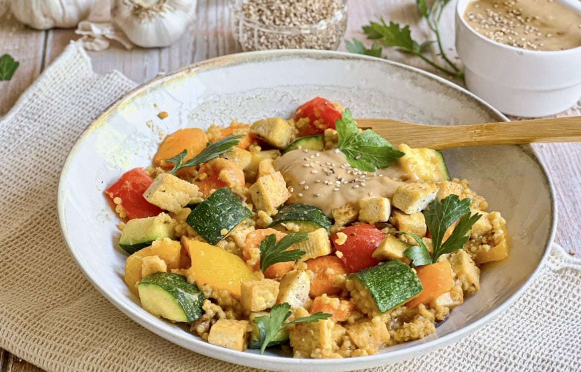 Vegane Hirsepfanne mit Gemüse, Tofu und einer cremigen Tahin-Zitronen-Soße auf einem Teller.
