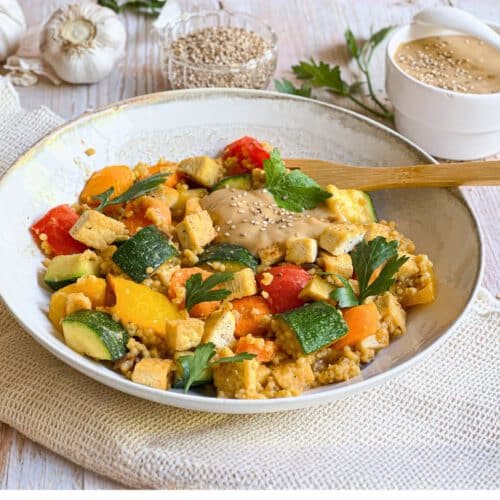 Vegane Hirsepfanne mit Gemüse, Tofu und einer cremigen Tahin-Zitronen-Soße auf einem Teller.