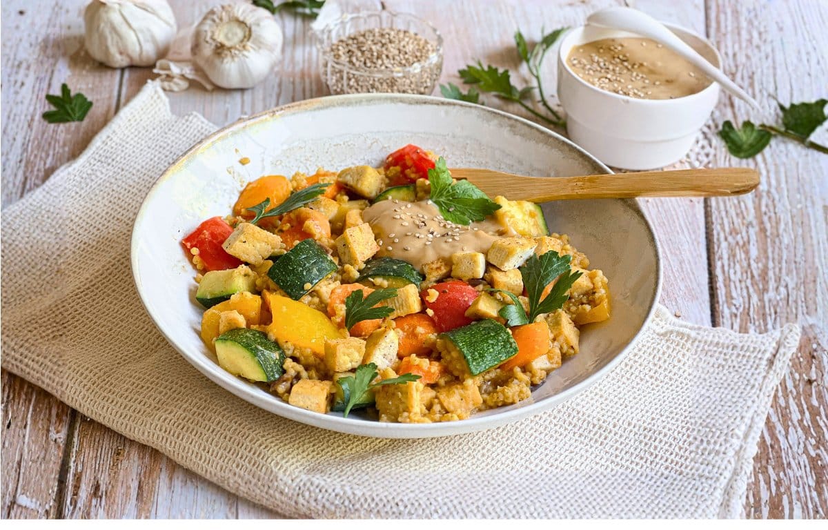 Vegane Hirsepfanne mit Gemüse, Tofu und einer cremigen Tahin-Zitronen-Soße auf einem Teller.