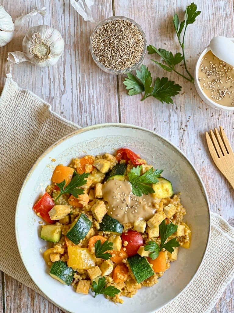 Vegane Hirsepfanne mit Gemüse, Tofu und einer cremigen Tahin-Zitronen-Soße auf einem Teller.