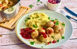 Vegane Köttbullar mit Rahmsoße, Preiselbeeren und Kartoffelstampf auf einem Teller.