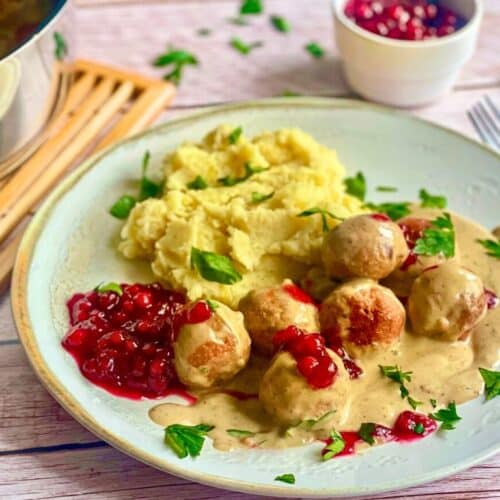 Vegane Köttbullar mit Rahmsoße, Preiselbeeren und Kartoffelstampf auf einem Teller.