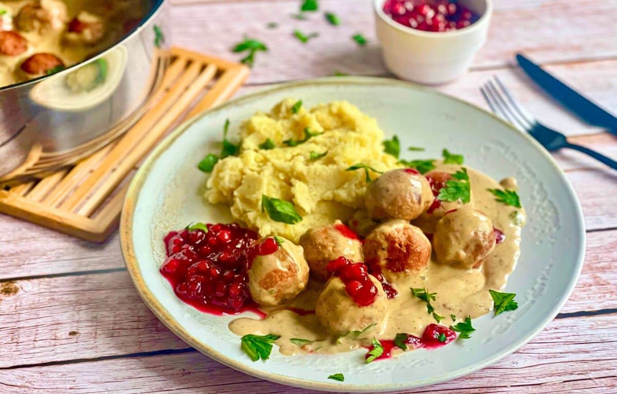 Vegane Köttbullar mit Rahmsoße, Preiselbeeren und Kartoffelstampf auf einem Teller.