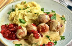 Vegane Köttbullar mit Rahmsoße, Preiselbeeren und Kartoffelstampf auf einem Teller.