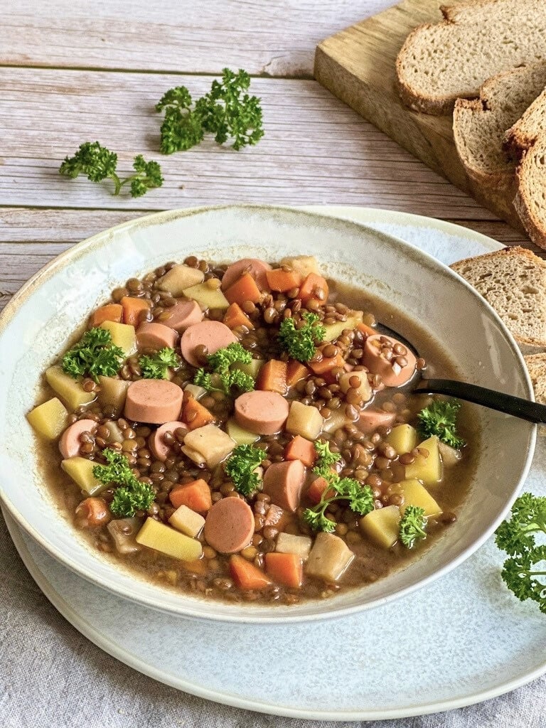 Vegane Linsensuppe mit Würstchen in einem Suppenteller.