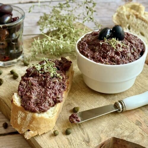Vegane Oliventapenade auf einem Holzbrett.