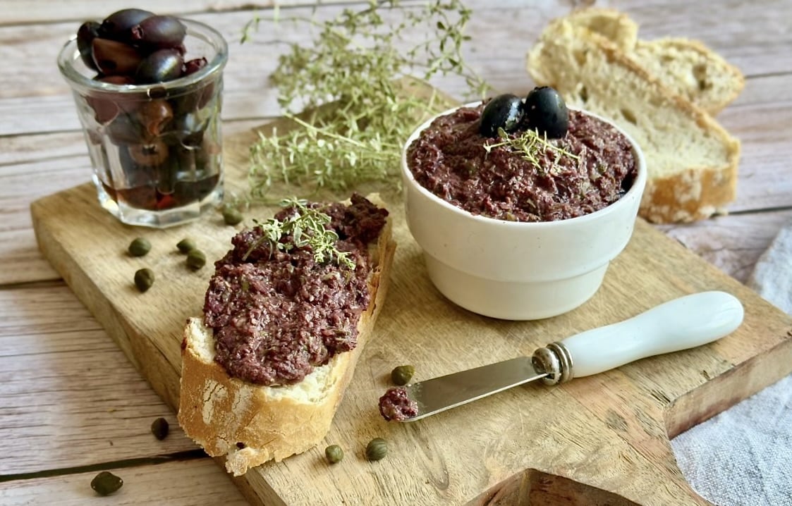 Vegane Oliventapenade auf einem Holzbrett.