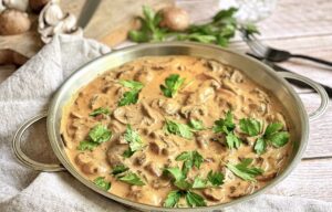 Vegane Rahmchampignons mit Petersilie in einer Pfanne auf einem Tisch.