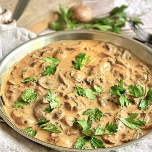 Vegane Rahmchampignons mit Petersilie in einer Pfanne auf einem Tisch.