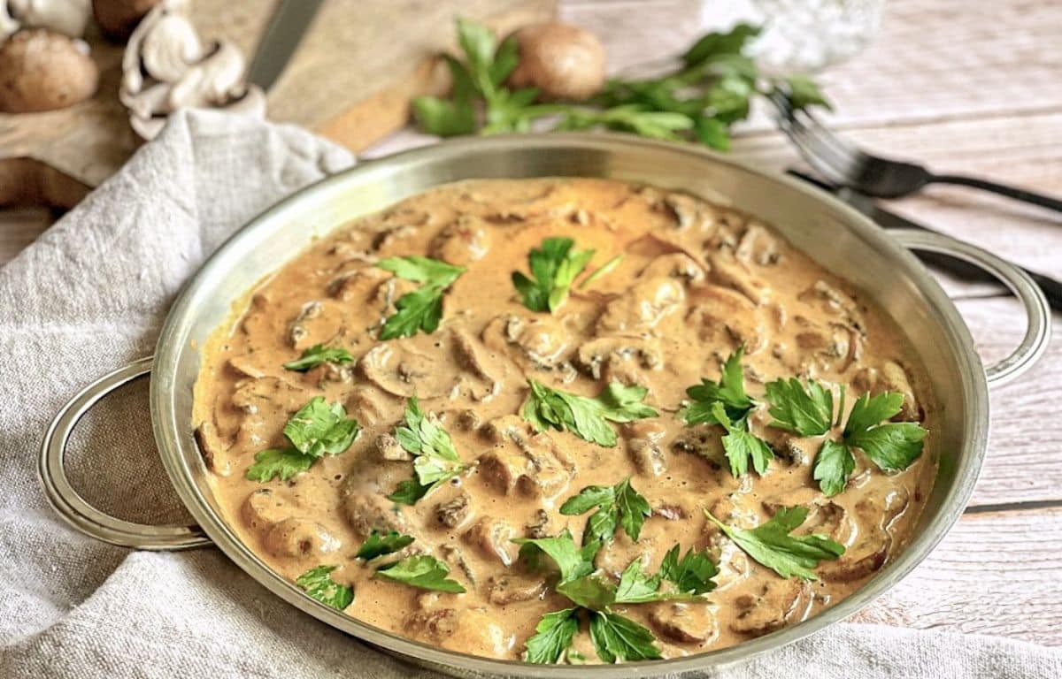 Vegane Rahmchampignons mit Petersilie in einer Pfanne auf einem Tisch.