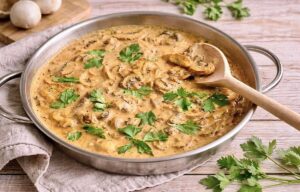 Vegane Rahmchampignons mit Petersilie in einer Pfanne auf einem Tisch.