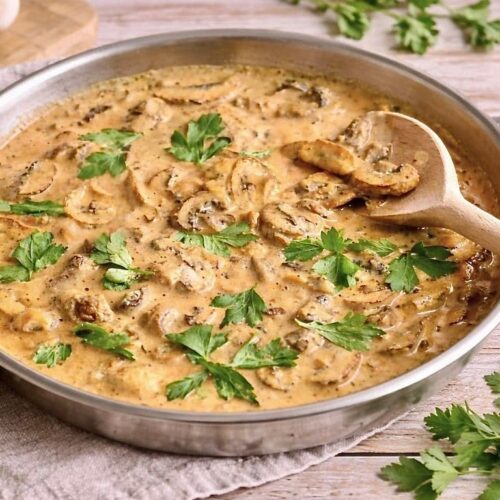 Vegane Rahmchampignons mit Petersilie in einer Pfanne auf einem Tisch.