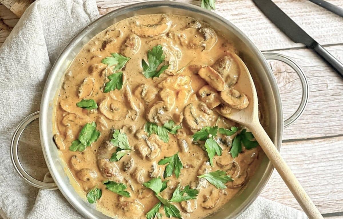 Vegane Rahmchampignons mit Petersilie in einer Pfanne auf einem Tisch.