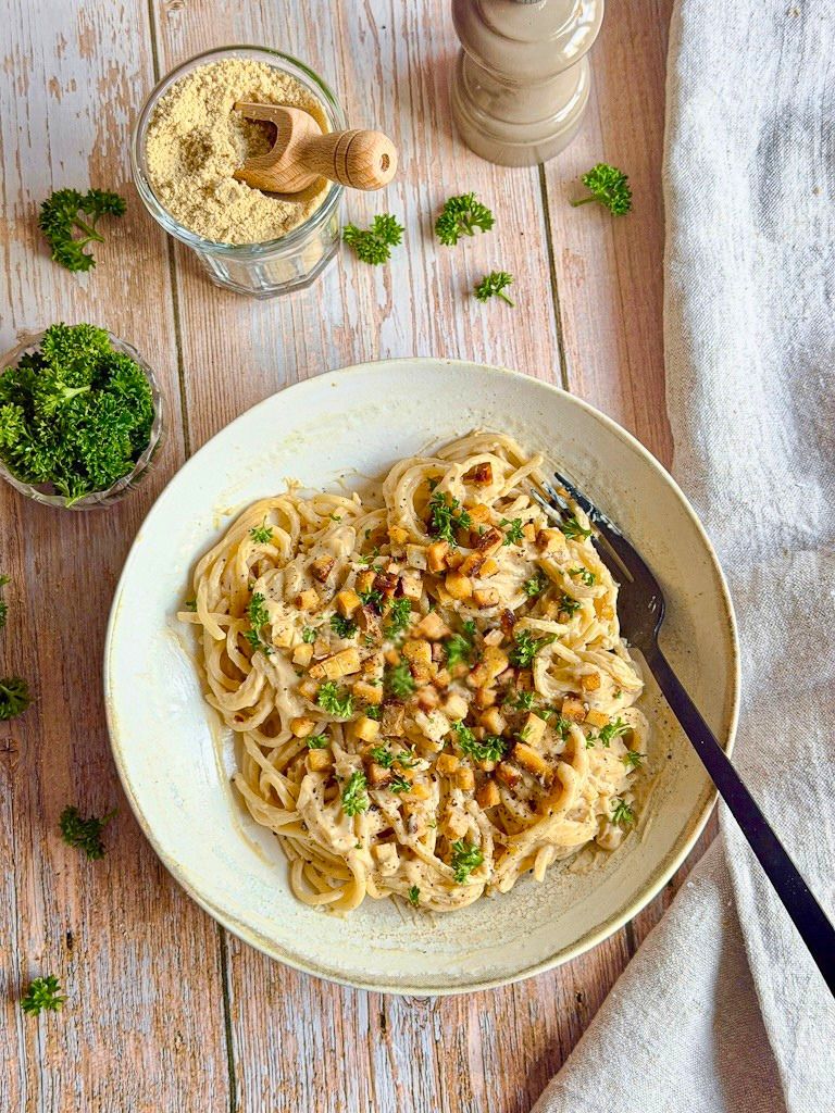 Cremige vegane Spaghetti Carbonara mit Petersilie auf einem Teller.