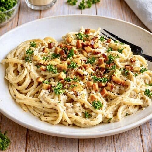Vegane Spaghetti Carbonara mit Petersilie auf einem Teller.