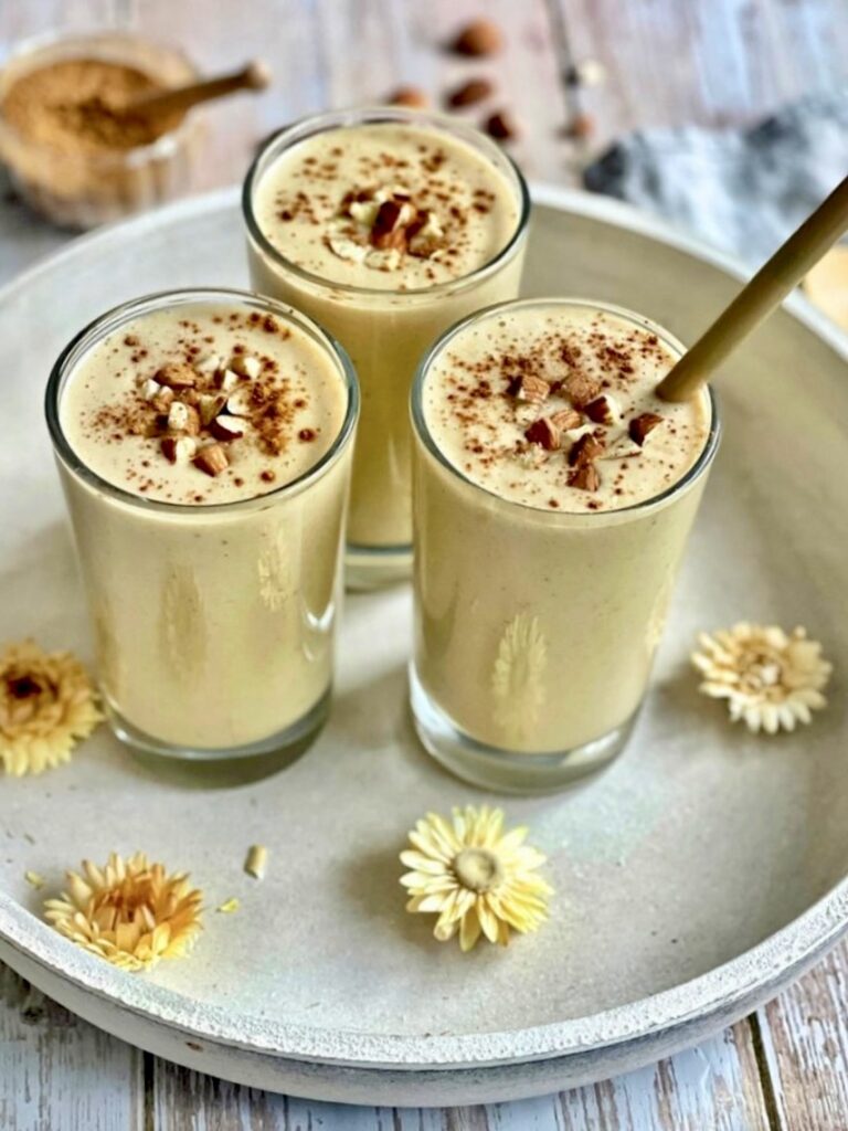 Veganer Bananenshake mit Mandeln und Zimt in drei Gläsern auf einem Tablett.