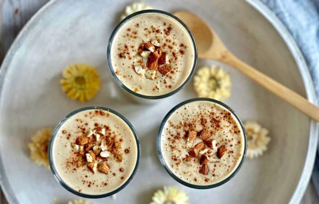 Veganer Bananenshake mit Mandeln und Zimt in drei Gläsern auf einem Tablett.