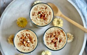 Veganer Bananenshake mit Mandeln und Zimt in drei Gläsern auf einem Tablett.