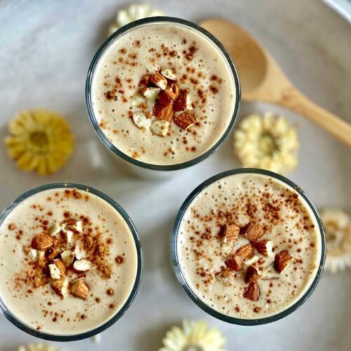 Veganer Bananenshake mit Mandeln und Zimt in drei Gläsern auf einem Tablett.