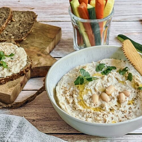 Veganer Bohnenaufstrich in einer Schüssel mit Rohkoststicks und Vollkornbrot.