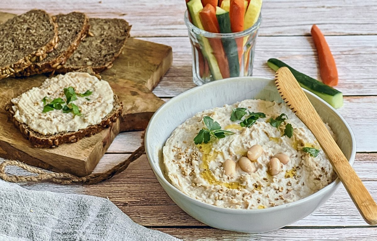 Veganer Bohnenaufstrich in einer Schüssel mit Rohkoststicks und Vollkornbrot.