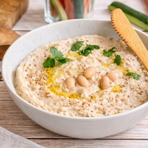 Veganer Bohnenaufstrich in einer Schüssel mit Rohkoststicks und Vollkornbrot.