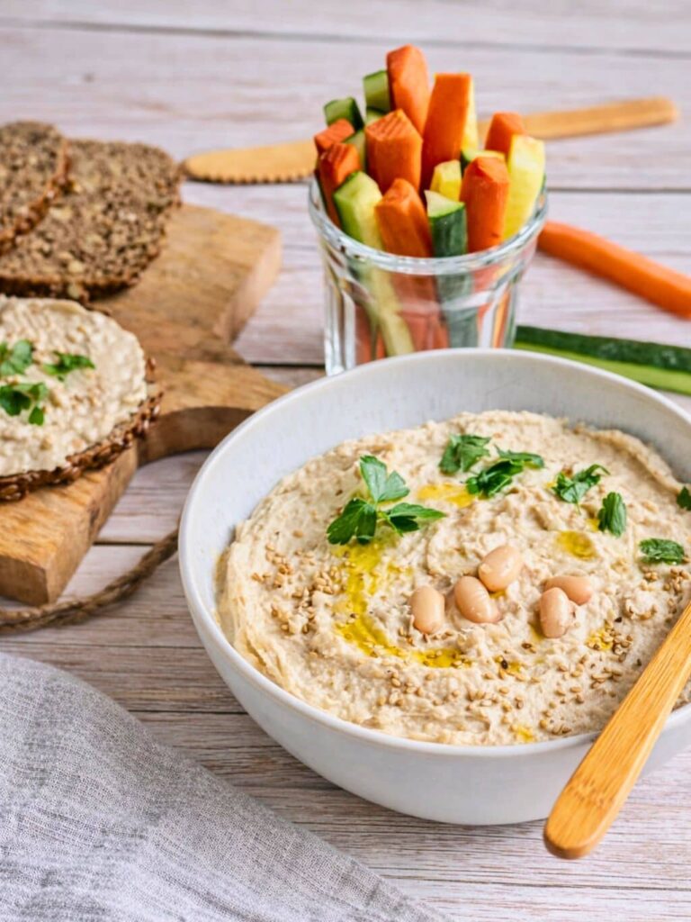 Veganer Bohnendip in einer Schüssel mit Rohkoststicks und Vollkornbrot.